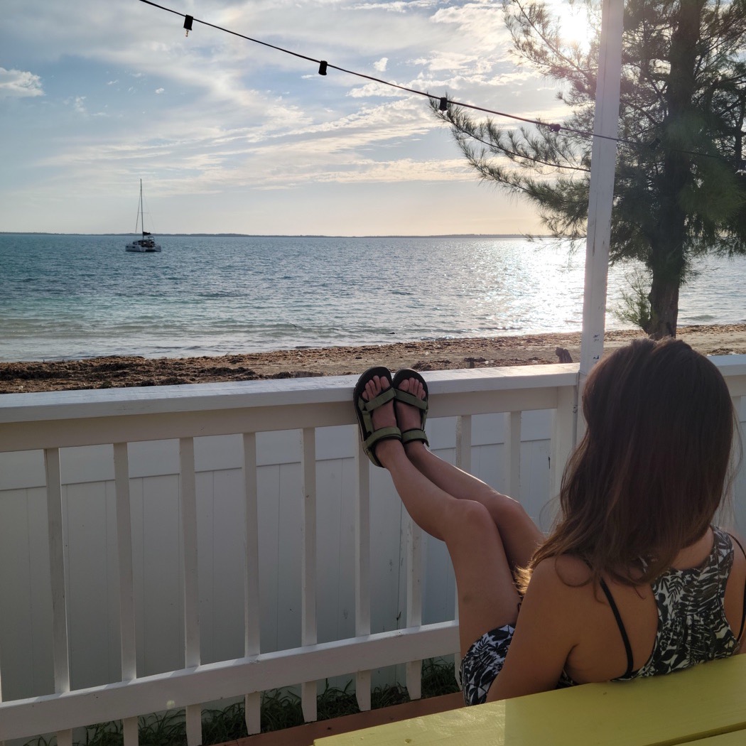 Feet up on a porch rail looking out at the water and a sailboat